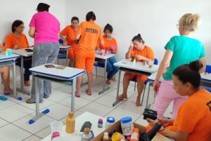 sala com internas vestidas de laranja participando de oficina de artesanato.