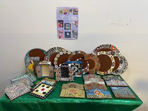 mesa forrada de verde com peças artesanais em mosaico, entre quadros e pratos.