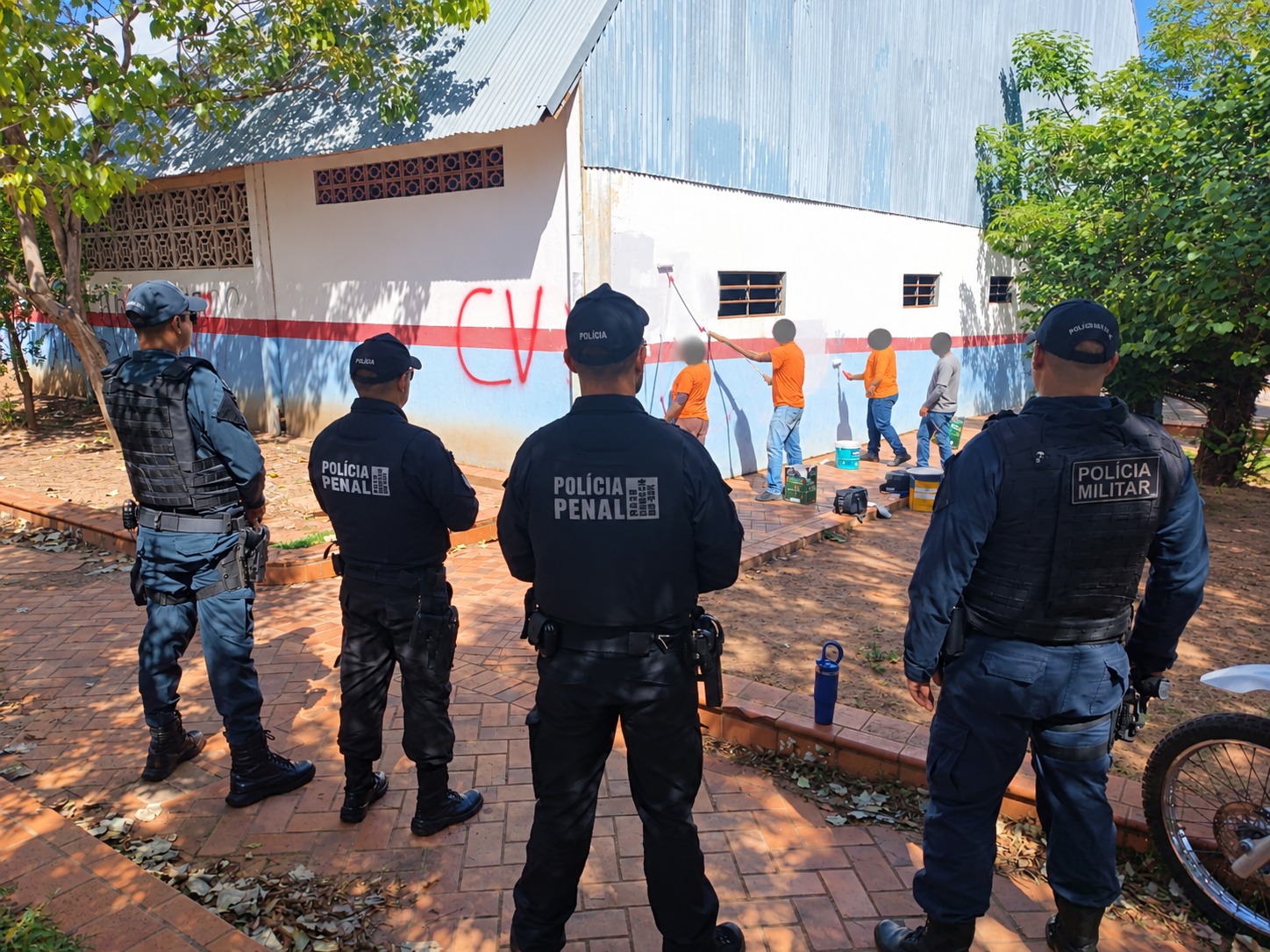 Policiais penais e militares fazem a segurança enquanto internos cobrem as pichações