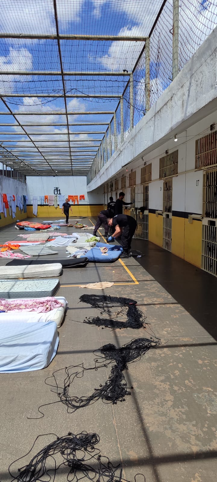 Policiais penai inspecionam colchoes em patio de presídio.